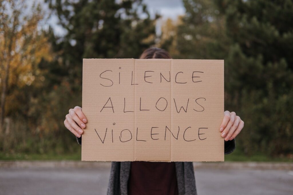 Person holding a sign that reads "Silence Allows Violence"
