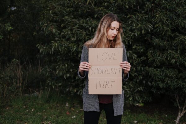 Woman holding a sign reading "Love shouldn't hurt."