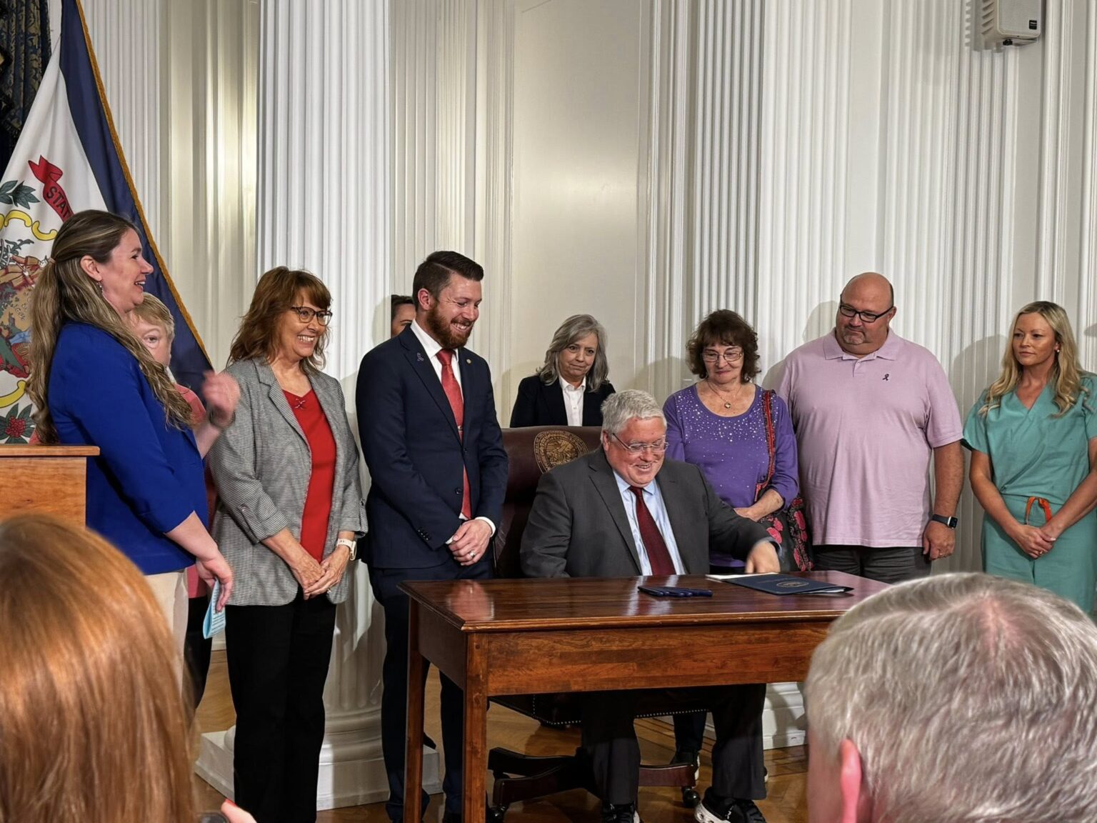 Governor Morrissey sits at a desk, people are gathered for the bill signing
